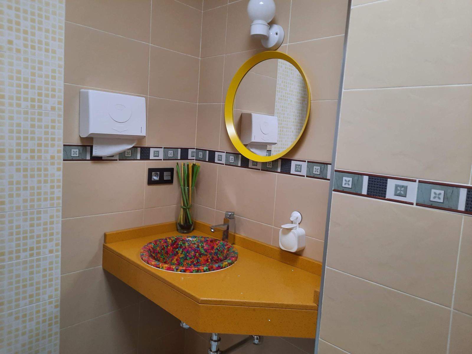 Detalle de lavabo amarillo con espejo redondo en baño de clínica